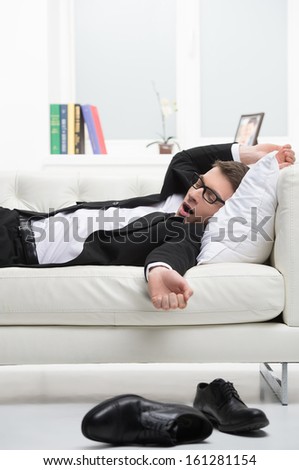 Man sleeping on a couch in business suite. With black classical shoes on foreground 