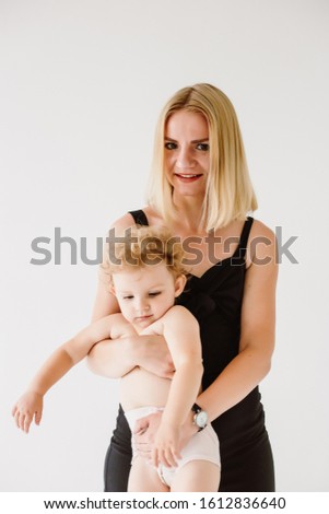 Beautiful fashion Mom blonde in a black fashion suit holds in her hands a little two-year-old daughter, on a white background