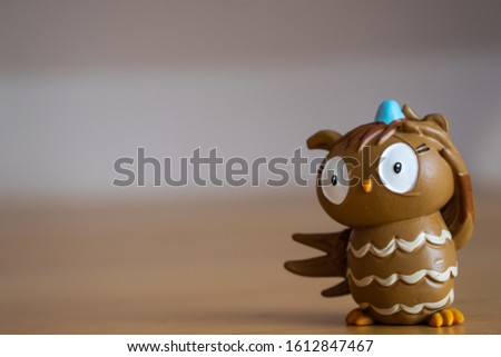 A brown funny owl character standing on a wooden table with a blurry background