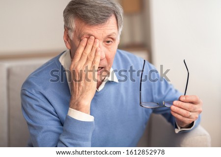 Glaucoma. Tired Elderly Man Massaging Eye Holding Eyeglasses Having Eyestrain And Ocular Tension Sitting On Couch At Home. Selective Focus Royalty-Free Stock Photo #1612852978