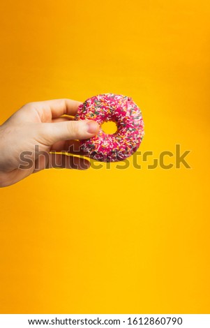 Donut with pink icing in hand on yellow background