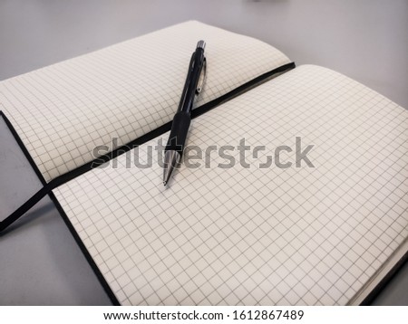 A black pen on a square ruled notebook against a white background