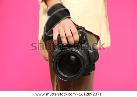 Professional photographer with modern camera on pink background in studio, closeup