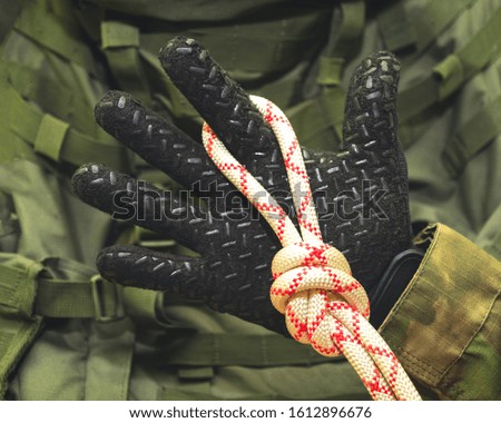 hand in a black glove holds a climbing rope tied in a knot "eight" on the background of a military backpack