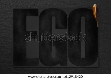 Burning piece of black paper with the word "EGO"on a black background.