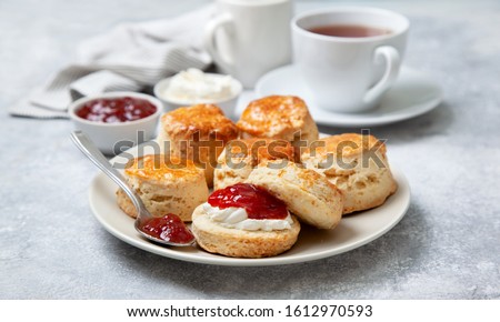 scones on a white plate, a jar of strawberry jam and a cup of tea on a gray background Royalty-Free Stock Photo #1612970593