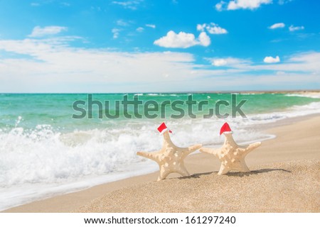 Sea-stars couple in red santa hats walking at sea beach. New Years day and Christmas vacation concept.