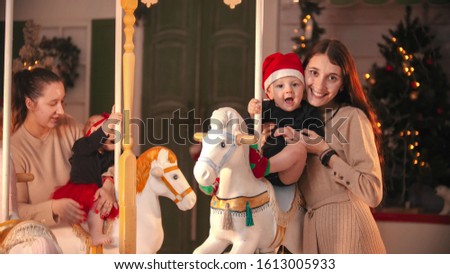 Having fun with christmas decoration - two smiling mothers standing near the carousel with their babies