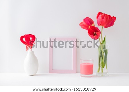 Home interior with decor elements. Mockup with a pink frame, red tulips in a vase on a light background