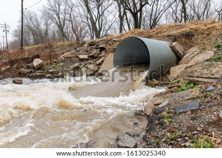 Closeup motion blur of storm water runoff flowing through metal drainage culvert under road. January storms brought heavy rain and flash flooding to Illinois Royalty-Free Stock Photo #1613025340