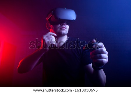 guy a gamer in modern wireless glasses of virtual reality plays a shooter, a man is focused on a 3D game in a dark room Royalty-Free Stock Photo #1613030695