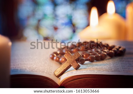 Rosary beads and crucifix cross on holy bible with candles in church Royalty-Free Stock Photo #1613053666