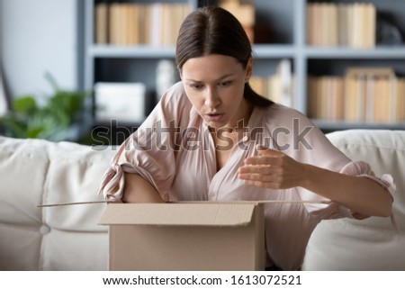 Frustrated young woman sit on couch in living room unpack carton box with Internet order distressed with bad quality product, dissatisfied female buyer client open box shop online get damaged goods Royalty-Free Stock Photo #1613072521