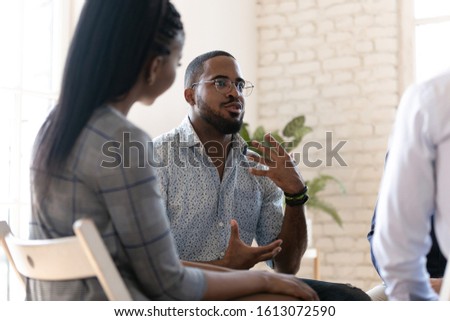 Excited african American man in glasses sit in circle at team therapy session talking sharing thoughts or ideas, motivated biracial male counseling diverse people at group psychotherapy treatment Royalty-Free Stock Photo #1613072590