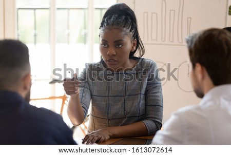 Serious african American young businesswoman hold lead meeting in office talk with male coworker, confident angry ethnic female team leader scold lecture coworker at briefing at workplace Royalty-Free Stock Photo #1613072614