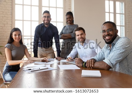 Portrait of happy diverse young businesspeople gather at boardroom table brainstorming discussing business ideas together, multiethnic millennial colleagues look at camera posing at meeting Royalty-Free Stock Photo #1613072653