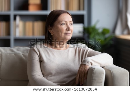 Pensive senior woman sit on sofa in living room look in window distance thinking pondering, thoughtful middle-aged female rest on couch at home lost in thoughts dreaming or remembering Royalty-Free Stock Photo #1613072854