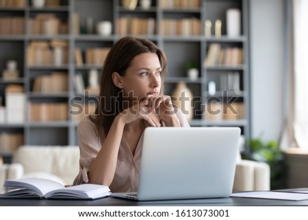 Pensive millennial girl sit at desk look in window distance thinking or dreaming visualizing, thoughtful young woman distracted from computer work pondering over problem solution, lost in thoughts Royalty-Free Stock Photo #1613073001
