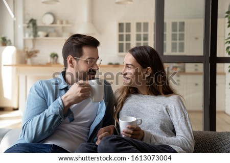 Happy young married couple enjoying cozy romantic weekend time with cup of hot tea coffee chocolate. Smiling pleasant family spouse relaxing on sofa, heart-to-hear talk, spending evening together. Royalty-Free Stock Photo #1613073004