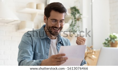 Head shot happy young man winner in eyeglasses reading paper letter with good news, making yes gesture. Joyful bearded guy celebrating personal achievement or banking loan approval, taxes refund. Royalty-Free Stock Photo #1613076466