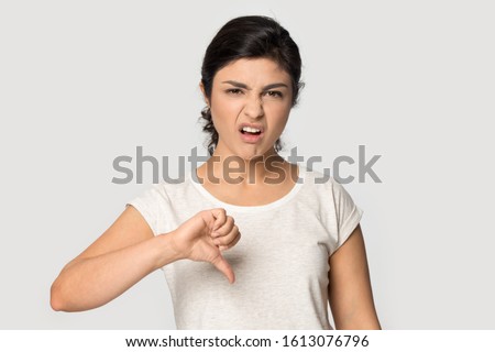 Dissatisfied bored unhappy young indian ethnicity female client giving negative feedback about product or service isolated on grey studio background. Millennial customer demonstrating dislike gesture.
