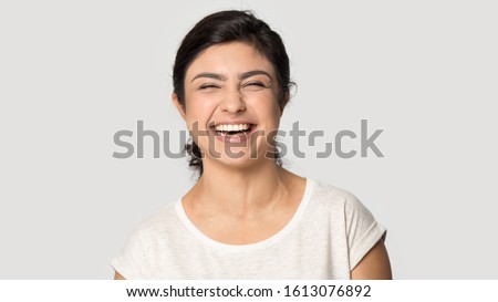Head shot close up studio portrait millennial funny attractive indian ethnicity woman feeling excited, joyful, sincerely laughing at joke, expressing positive emotions isolated on grey background.