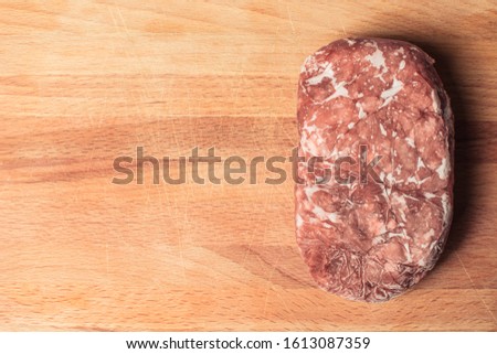 Piece of frozen minced pork for cooking beefsteak on cutting board