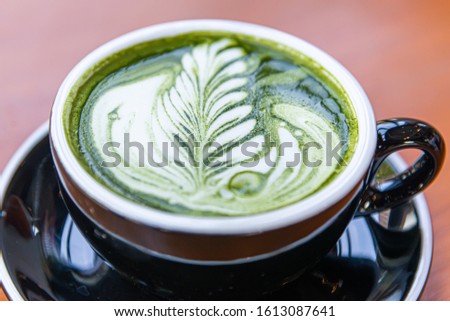 Close up pattern of black cup of matcha latte green tea on wooden table.