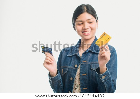 Portrait of a pretty young woman dressed in denim shirt holding credit card at her face isolated over white background. - Image