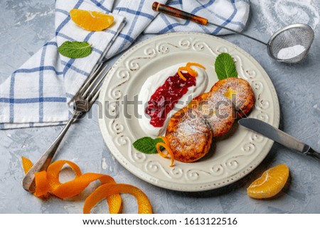 Homemade cottage cheese pancakes with cowberry jam and sour cream in a white plate on a gray textured background. Top view.