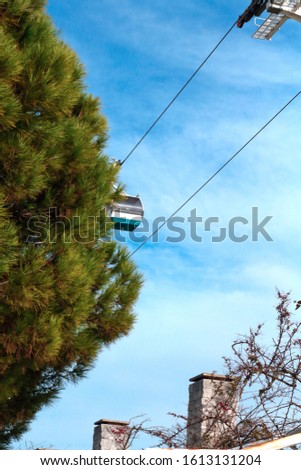 Small electric funicular cabins in the blue sky above the promenade near the park with green trees in summer. Telecabina 