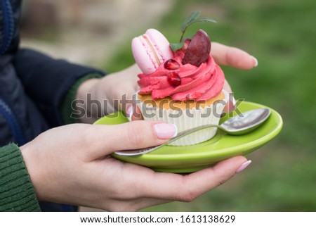 Woman holds a saucer with  beautiful and healthy cupcake decorated macaron and grape, picture taken outdoor in spring.