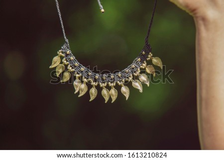 Macrame necklace with brass leaves pendants hanging on natural background bokeh
