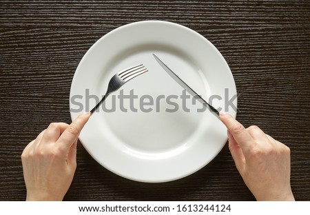Fork and knife in hands on wooden background with white plate Royalty-Free Stock Photo #1613244124