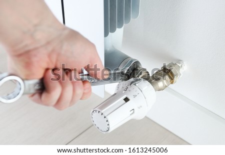 Worker hands repairing radiator with wrench. Close-up.Removing air from the radiator and fixing a heating problem.Dismantling and repair of a heating radiator in a house, apartment.Heating off. Royalty-Free Stock Photo #1613245006