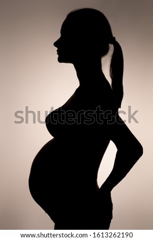silhouette of a pregnant woman with ponytail hair holding one hand on her lower back