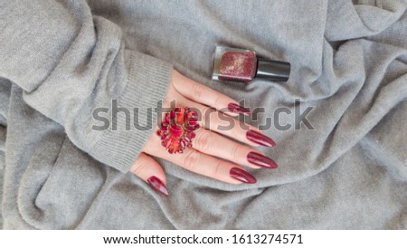 Female hand with long nails and a bottle of dark red nail polish