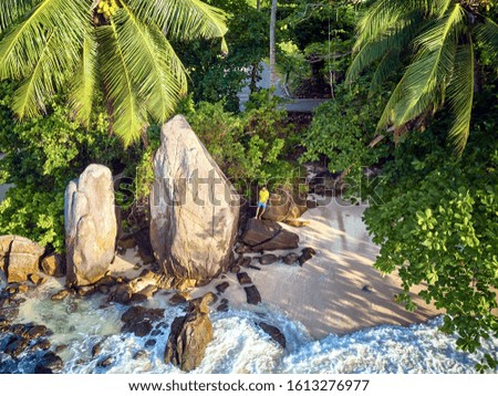 Man on beautiful beach with palm tree and rocks aerial top view drone shot at Seychelles, Mahe