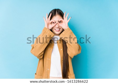 Young chinese woman posing in a blue background isolated showing okay sign over eyes