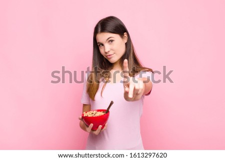 young pretty woman smiling proudly and confidently making number one pose triumphantly, feeling like a leader with a breakfast bowl