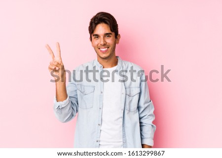 Young caucasian man posing in a pink background isolated joyful and carefree showing a peace symbol with fingers.