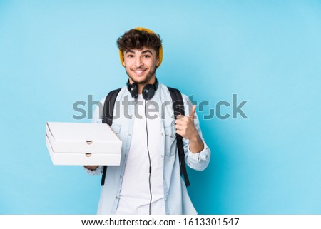Young arab student man holding pizzas isolated smiling and raising thumb up
