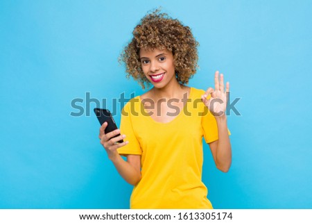 young african american feeling happy, relaxed and satisfied, showing approval with okay gesture, smiling with a mobile phone