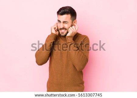 Young caucasian man against a pink background isolated covering ears with hands.