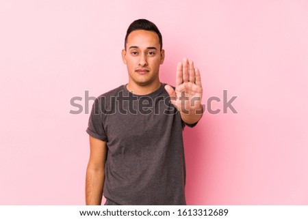 Yooung latin man posing in a pink backgroundstanding with outstretched hand showing stop sign, preventing you.