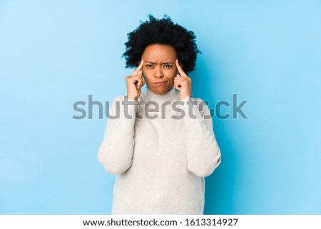 Middle aged african american woman against a blue background isolated focused on a task, keeping forefingers pointing head.