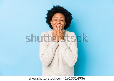 Middle aged african american woman against a blue background isolated laughing about something, covering mouth with hands.