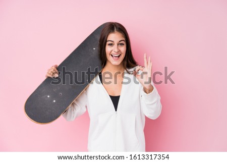 Young caucasian skater woman holding skate cheerful and confident showing ok gesture.