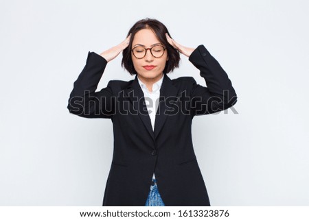 young businesswoman looking concentrated, thoughtful and inspired, brainstorming and imagining with hands on forehead against white wall