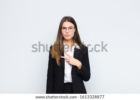 young businesswoman feeling happy, positive and successful, with hand making v shape over chest, showing victory or peace against white wall